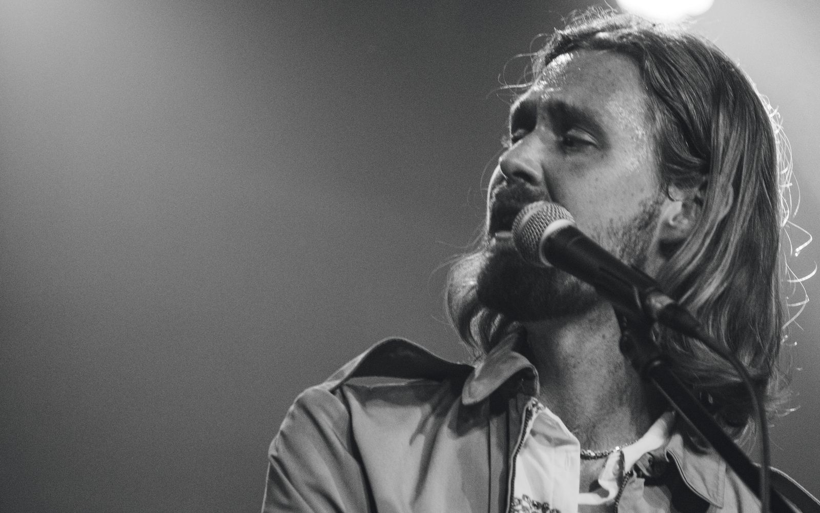 Tobias Lund singing into the mic at the keys under a stage light, in black and white